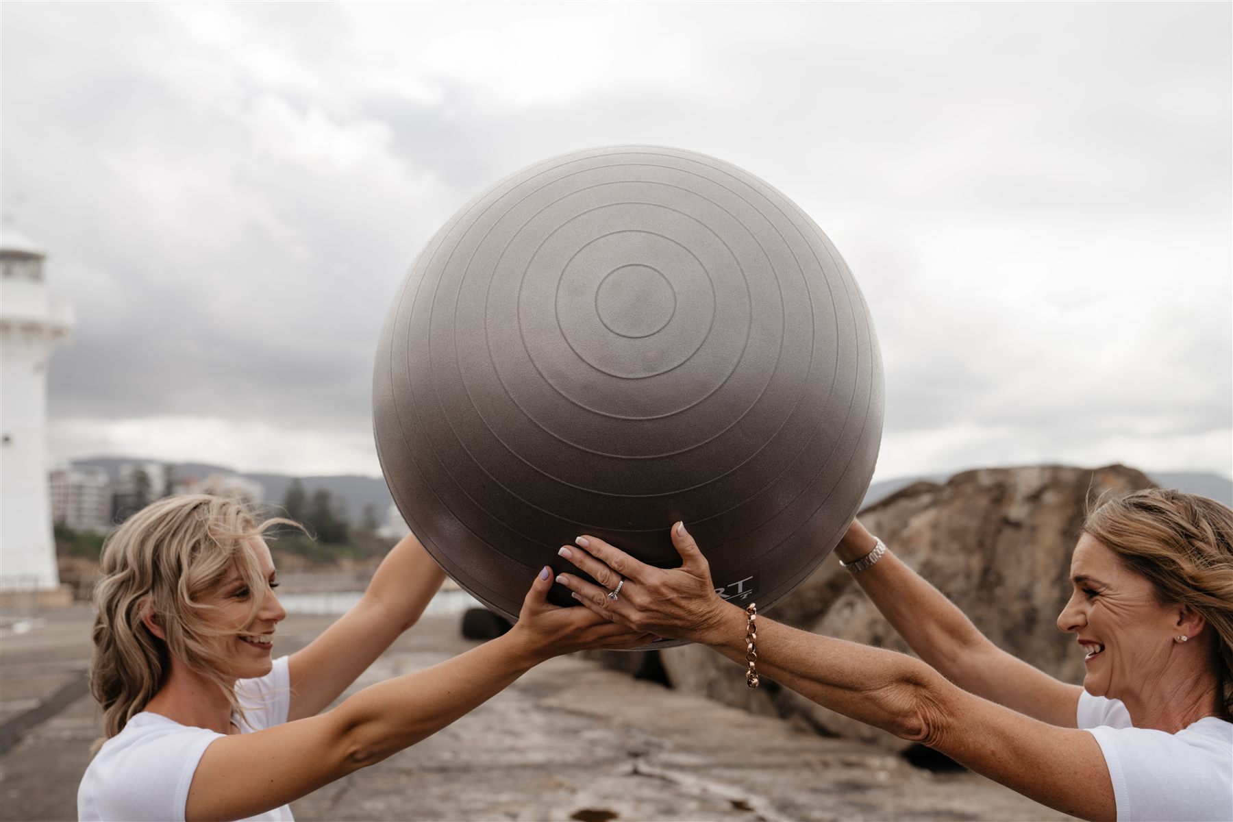 Two clients lifting an exercise ball together in a Pilates Comes To You movement session